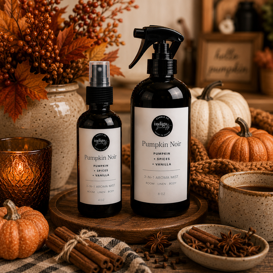 Two dark amber spray bottles labeled Hedgesley Pumpkin Noir room and body care products, styled on a wooden tray with autumn decor including pumpkins, a candle, cinnamon sticks, and a mug.