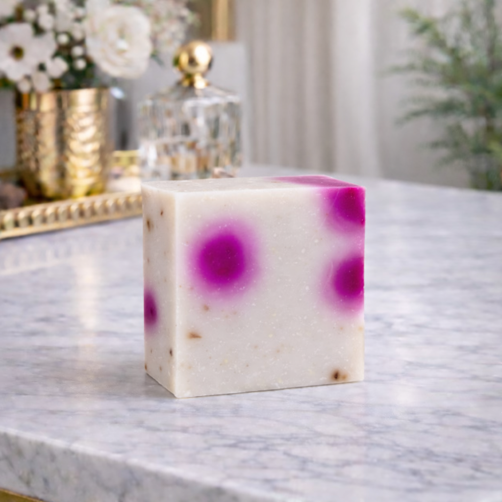 Bar of soap with purple speckles on a marble surface, decorative items in the background
